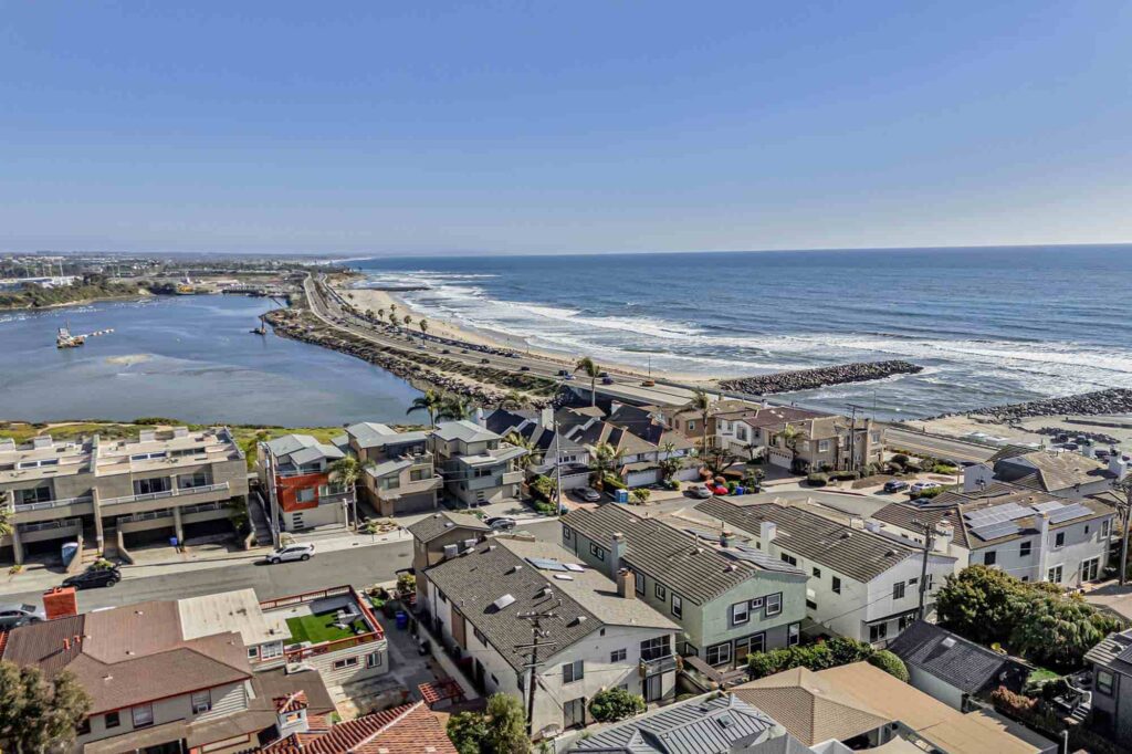 Aerial view of Carlsbad coastline showing beachfront homes Aerial view of Carlsbad coastline showing beachfront homes, a narrow coastal road and jetties sheltering a lagoon as waves roll into the shore under a clear blue sky