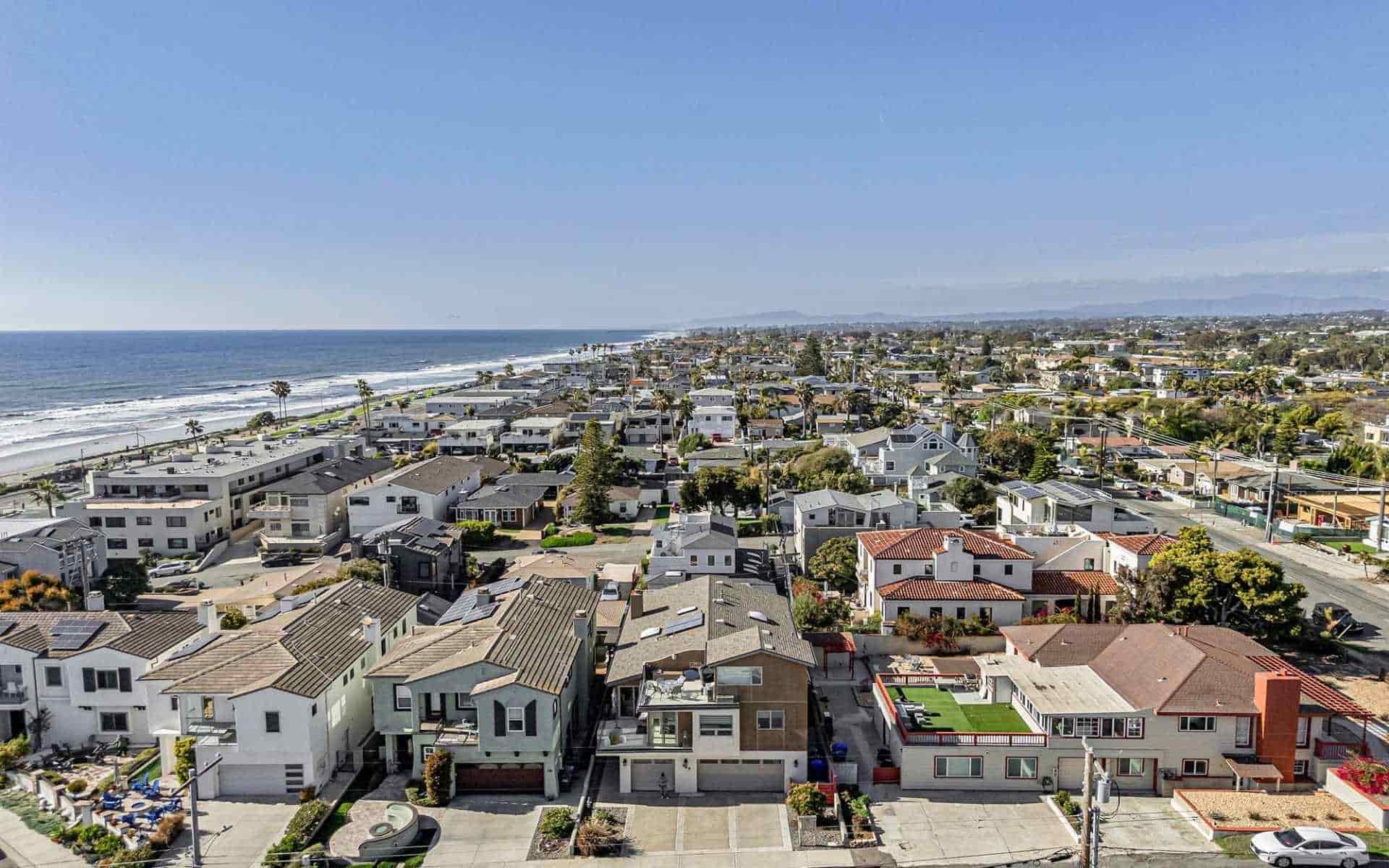 Aerial view of Carlsbad, California showing beachfront homes and coastal neighborhoods stretching along the shoreline with the ocean on the left.