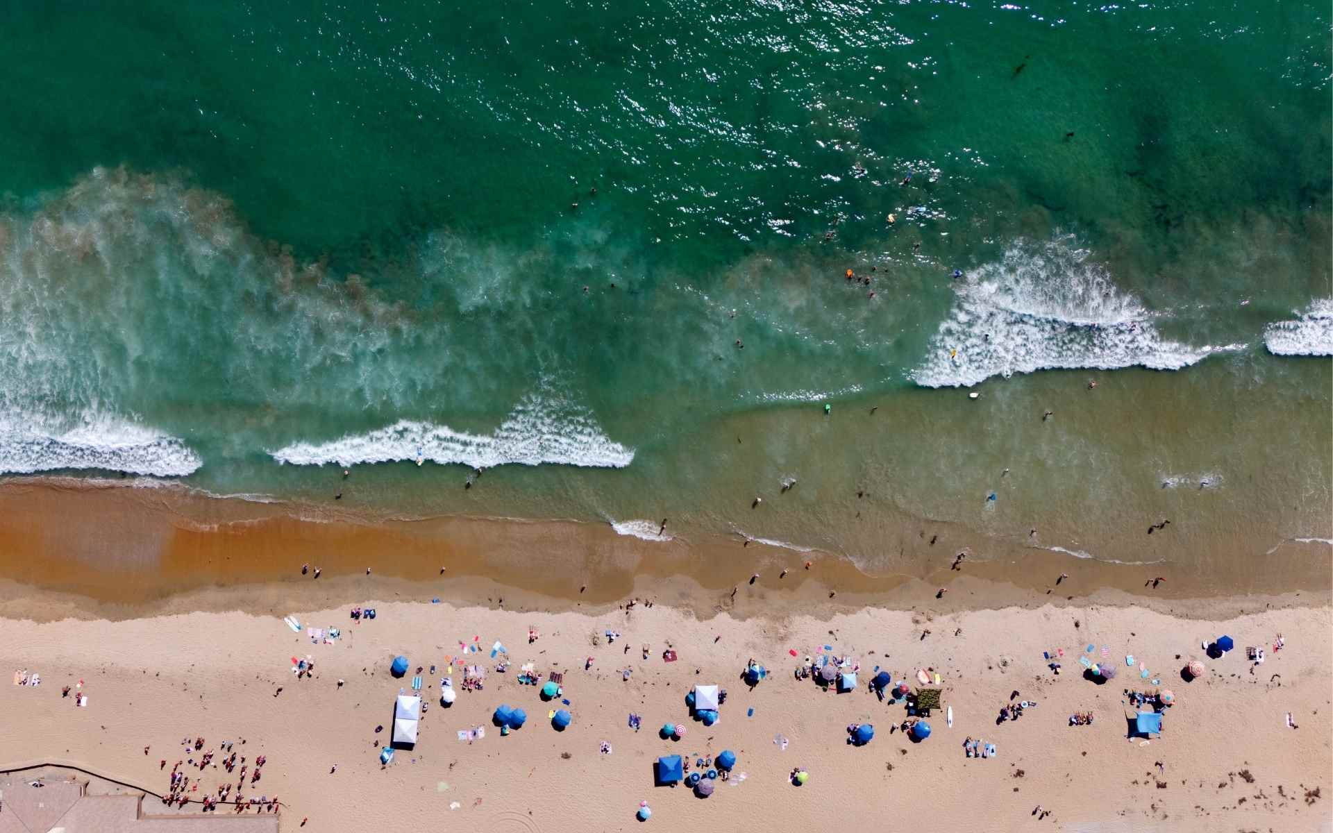 Aerial view of San Clemente coastline showing the sandy beach, surfers in the water, and people on the shore.