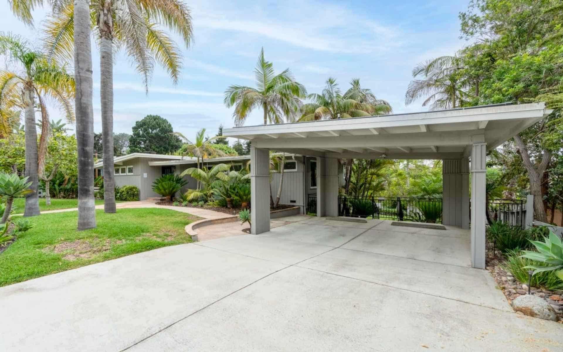 Solana Beach vacation rental managed by thecoastalproject.com — concrete driveway leads to a covered carport, surrounded by palm trees and lush tropical landscaping. (property managed by thecoastalproject.com)