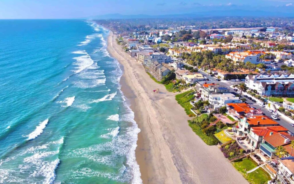 Carlsbad Oceanfront Homes Beach Aerial View Coastal Vacation Rentals Aerial view of Carlsbad beach in California with turquoise waves rolling onto a wide sandy shoreline, lined with oceanfront homes and coastal neighborhoods on a clear day