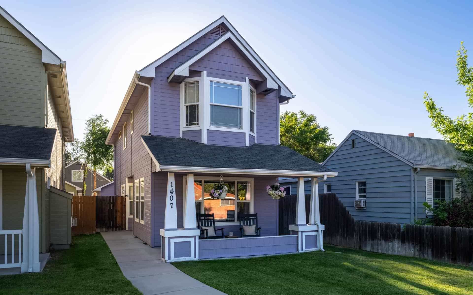 Two-story lavender home with white trim, a covered front porch, and a green lawn between neighboring houses.
