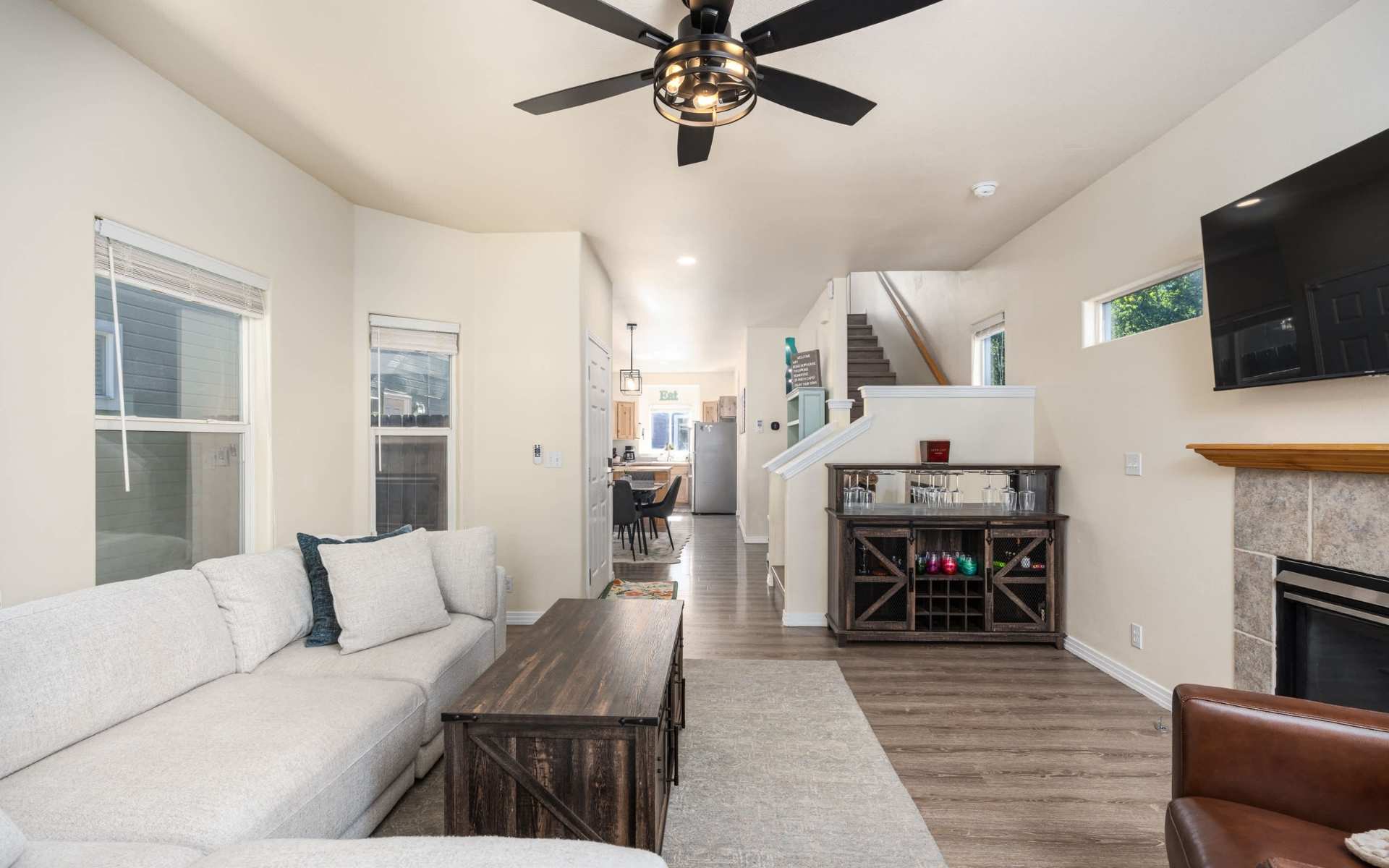Furnished living room with a light sofa, wooden coffee table, fireplace, wall-mounted TV, and an adjoining kitchen.
