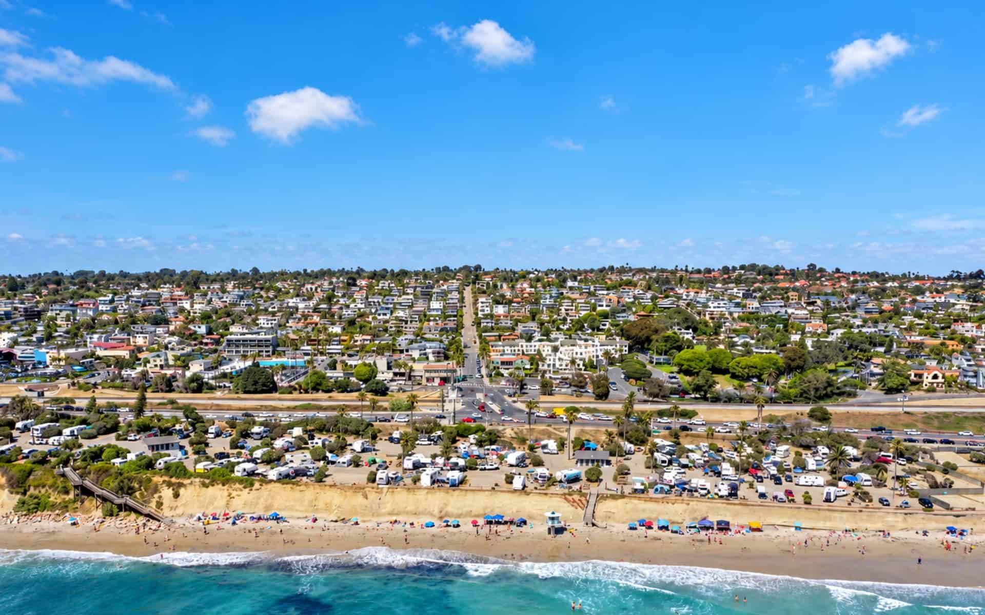 Aerial view of Cardiff-by-the-Sea homes behind a beachfront campground, with ocean waves in the foreground.