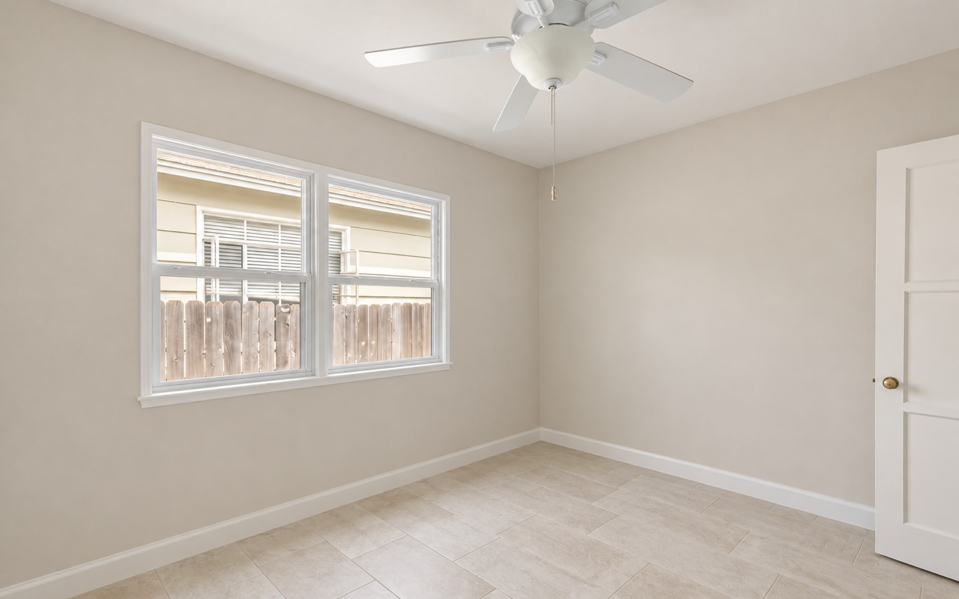 Unfurnished bedroom with neutral walls, pale tile flooring, two windows, and a white ceiling fan.