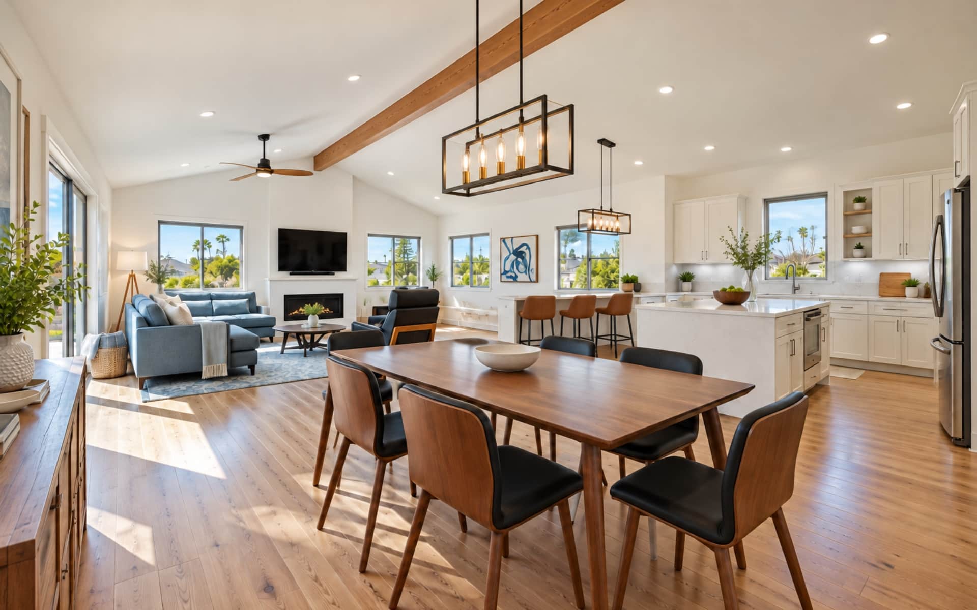Open-plan home with a walnut dining table, blue-gray sofa, white kitchen, and vaulted ceiling with an exposed wood beam.
